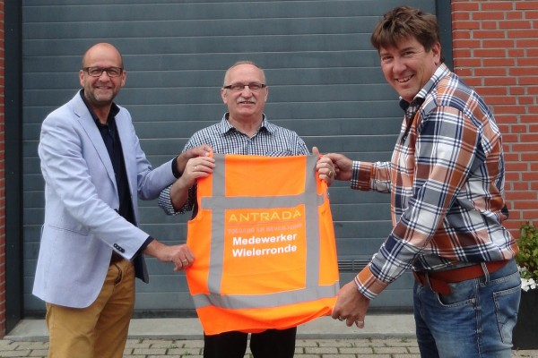 Op de foto overhandigen Arjan in’t Veld, commercieel directeur, (links) en Ed Groenendijk, technisch directeur (rechts) de vestjes aan Arie van Driel, bestuurslid van de Wielerronde van Alblasserdam.